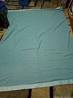 Full view of the light blue wool blanket laid flat showing size and satin trim edges.
