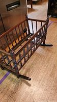 Full view of antique wooden spindle crib showing side and rockers on a wooden floor.