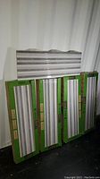 Four green boxes each containing six long rectangular contemporary ceramic wall tiles with textured horizontal grey and white stripes, stacked against a corrugated surface.