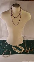 Photo showing multiple necklaces displayed on a white bust and laid flat on a cloth, capturing the assortment of jewelry pieces