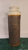 Side view of the tall cylindrical MCM pottery vase showing the cream top glaze with rust speckles and the textured brown spiral design along the body.