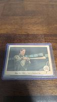 Photo of 1959 Ted Williams baseball card in plastic sleeve showing image of Ted Williams holding a bat horizontally with text date May 16, 1954 and caption.