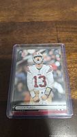 Brock Purdy rookie football trading card in protective sleeve showing front of card with player image and rookie logo.