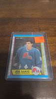 Joe Sakic rookie hockey card in protective sleeve on wooden surface, showing front of card with player image and team logo.
