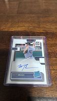 Close-up of Matt Brash rookie autograph baseball card in protective plastic holder on wooden surface