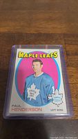 Front view of Paul Henderson hockey card from Toronto Maple Leafs inside a plastic protective case, showing colorful vintage card artwork with player image and team branding.