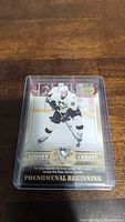 Close-up photo of Sidney Crosby rookie hockey card in a protective plastic case, showing him skating with the puck in Pittsburgh Penguins white jersey.