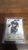 Sidney Crosby rookie hockey card in protective sleeve showing front with Pittsburgh Penguins uniform and Phenomenal Beginning text.