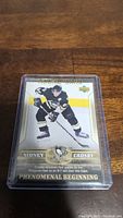 Sidney Crosby rookie hockey card in protective plastic case, showing player in Pittsburgh Penguins uniform, card number 87/76 and 'Phenomenal Beginning' subtitle.