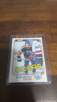 Photo of a Wayne Gretzky hockey card from Topps featuring him in Edmonton Oilers attire, inside a protective plastic case.