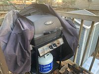 Broil-Mate gas BBQ grill covered partially with a black protective cover showing the propane tank underneath and front control panel.
