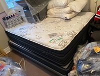 Overall view of mattress on platform bed with stacked pillows and surrounding items