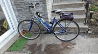 Full side view showing blue step-through frame, front suspension, wheels, handlebar bag, rear rack bag