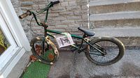 Full view of green child size bicycle showing frame, handlebars, curtains with scratches and dirt.