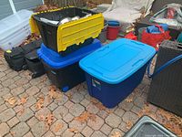 Three stacked storage bins shown outdoors on a paved surface surrounded by fallen leaves.