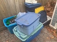 Photo showing stacked plastic storage bins of various colors and sizes, outdoors beside wooden fence.