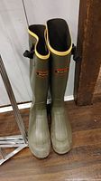 Full front view of tall olive green rubber boots with yellow trim and buckles.