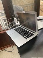 Angled view of silver Apple MacBook Air on black table showing screen, keyboard and charger cables.