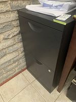 Side angle view of the black metal two-drawer filing cabinet showing overall shape, lock, and drawer handles.