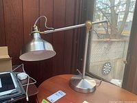 Side and front views of the metal desk lamp with flexible arm and conical shade, showing details of metal base, arm joints, and spring wire connection.