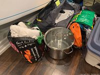 Photo showing large stainless steel pot, reusable tote bag with towels, and another tote bag with extra bags placed on wooden floor.