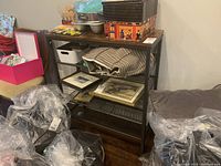 Frontal view of metal shoe rack showing wooden top and wire mesh shelves, surrounded by bags and other items.