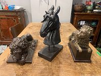 Photo showing two wood lion statues and one wood horse head statue arranged on a wooden table, with room cabinets in background.