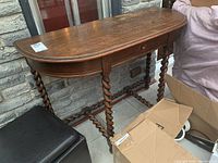 Side view of wooden demilune table showing twisted legs and single drawer with missing handle.