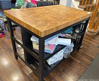 Side view of butcher block style table showing thick wood veneer top and open shelves filled with stored items.
