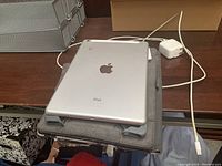 Apple iPad model A1475 placed on grey protective case and charger on wooden surface