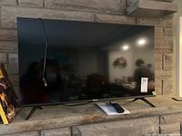 Front view of the 40-inch Hisense television on stand legs with power cord hanging and a user manual and remote control placed below.