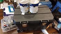 Photo of closed black Stanley rolling tool box, two large paint cans placed on top