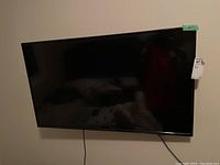 Front view of black flat-screen TV mounted on wall, showing screen and attached cables.