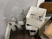 Pair of clear glass block lamps and dark metal lamp on floor next to white rectangular shades.