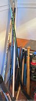 Baseball bats and hockey sticks grouped upright in corner showing taped grips, natural wood finishes, and composite materials.