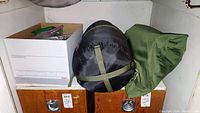 Photo showing the three storage bags and one box with camping gear items on a wooden cabinet.