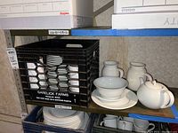 Shelf with white ceramic dishes, bowls, pitchers, and teapot from China Fair brand.