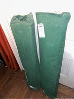 Two green canvas carry bags standing upright containing the two folding cots.