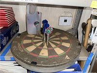 Dart board resting on shelf with some darts stuck in the board.