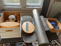 Overview of balance boards, foam rollers, exercise balls, and ankle weights in boxes on a table.