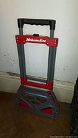Front view of folded Milwaukee hand truck showing folded platform and extendable handle with black padded grips.