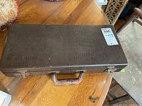 Closed brown hard case with textured exterior and worn leather handle.