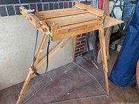 Full view of wooden painter's storage box easel with folding tripod legs on tiled ground.
