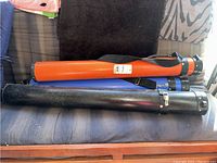 Three cylindrical art shipping tubes in orange, blue, and black, placed on a couch showing scratches and wear.