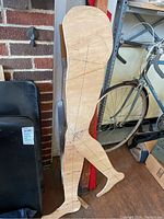 Wooden anatomical model of legs with measurement markings next to a bicycle and shelf in background.