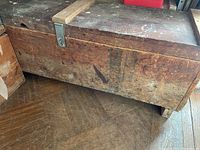 Large wooden trunk closed, showing weathered wood surface and metal latch on top