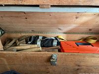 Photo showing inside of wooden trunk with several loose wooden pulleys, rope, black bag, and orange plastic case with carry handle.
