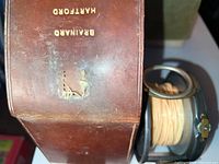 Brown leather slip case and fishing reel side by side