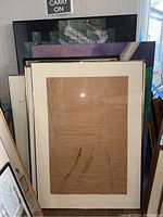 Stacked framed wall art showing front abstract drawing, screaming child painting, and map print behind