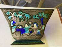 Side view of one face of the cloisonne dish showing multicolor enameled figures under trees with a turquoise background.